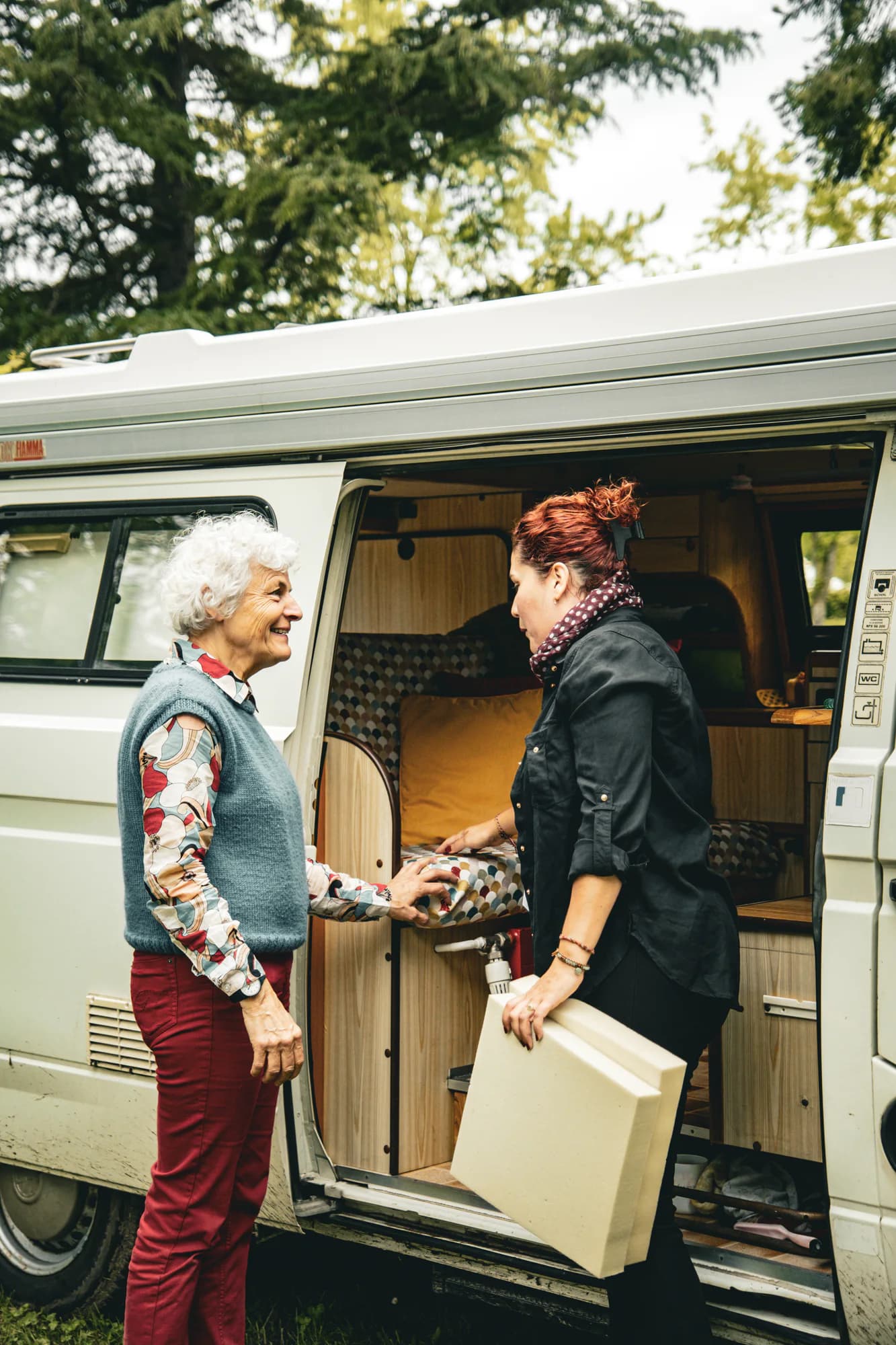 Échange autour d’un couchage et de blocs de mousse devant un camping-car.